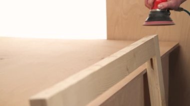 A front view of man's hand holding pneumatic power sander to polish a wood piece