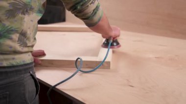 A side view of man's hand holding pneumatic power sander to polish a wooden frame.