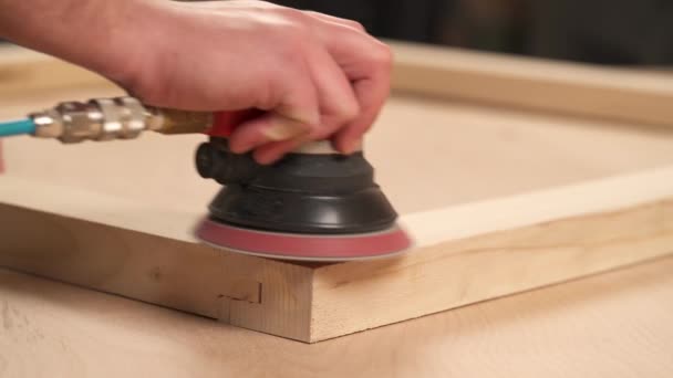 特写人的手拿着电动砂磨机 擦亮一个木制框架 并与花边木接头连接在一起 — 图库视频影像