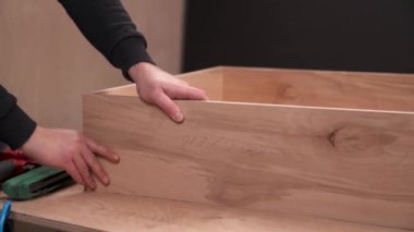 A front view of a carpenter joining work pieces with nail gun to make a wooden box