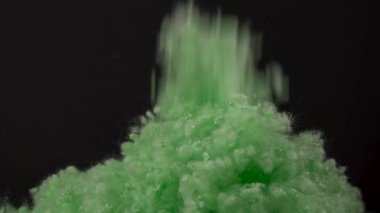 A close-up view of green synthetic fiber falling from up on the dark background