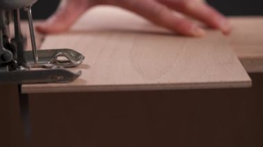 A side view of a power jigsaw cutting a piece of wooden board
