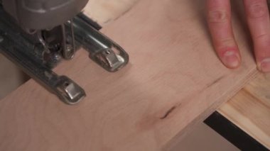 A view from top of a carpenter cutting with power jigsaw a piece of plywood board