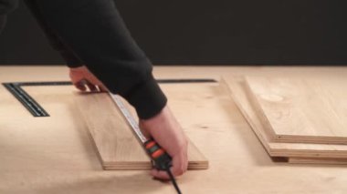A side view of man's hand holding a flexible ruler for measuring pieces of plywood. After carpenter is measuring workpieces with corner ruler