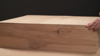 A front view of a man's hand covering a wooden box with a plywood board and stapling it with pneumatic staple gun