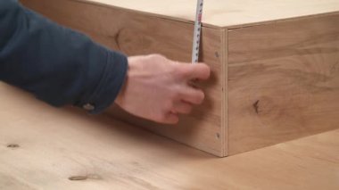 A close-up of man's hand holding a flexible ruler for measuring the height of wooden box