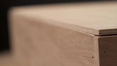 A close-up of man's hand holding a tape measure for measuring the length of wooden workpiece on the blurred background