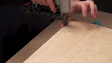 Elinde pnömatik zımba tabancası tutan ve tahta bir tahtayı tahta çekmeceye zımbalayan bir adamın elinden bir manzara.