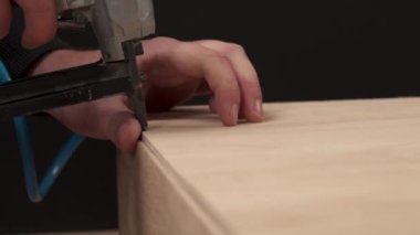 A side view of a man's hand holding pneumatic staple gun and stapling a plywood board to wooden drawer