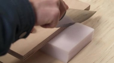 A side view of man's hand holding knife and cutting off a piece of furniture poly foam