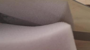 A side view of man's hand holding knife and cutting off a piece of furniture poly foam