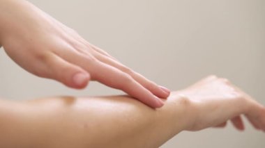 A close-up of a young woman rubs natural oil cosmetic product into the skin of her hands with gentle movements