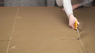 A tailor cutting a high quality brown fabric using professional scissors and squaring cut pieces of fabric