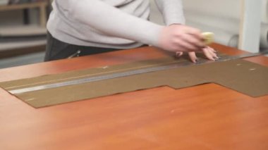 Profesyonel bir terzinin, cetvel kullanarak kahverengi malzemeyi tebeşirle şekillendirdiği bir yan görünüm. Materyali ölçüyor ve işaretliyor. Kesmeye hazırlıyor..