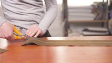 A front view of a tailor cutting a stripe of brown material using scissors
