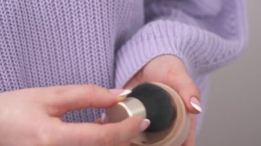 A front view of woman's hand holding a facial compact powder and putting the cosmetic brush into it