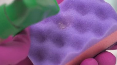 A close-up of spraying the detergent onto a purple sponge