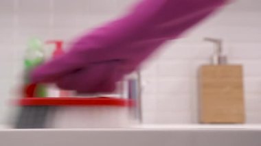 A close-up of woman's hand in pink rubber glove cleaning bathroom sink with a brush