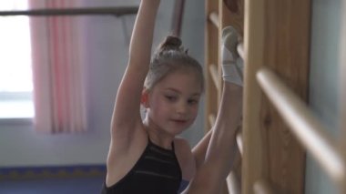 A close-up of a talented young athlete doing gymnastic exercises on wall bars with instructor (practicing the heel stretch)
