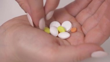 close-up view of young woman's hand holding vitamins and minerals pills. She is choosing and taking yellow ones