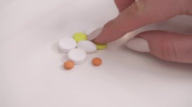 close-up view of vitamins and minerals pills lying on the white surface. Woman is choosing and taking yellow pills