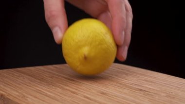 Yakın plan, bilinmeyen el ahşap masaya olgun limon koyar. Tüm sarı limon siyah arkaplanda izole edilmiş..