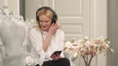 Beyaz bir el üzerinde oturan, koltuğu oyulmuş ve kulaklıkla müzik dinleyen çekici bir kadının ön görüntüsü.