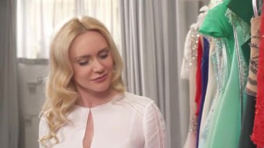 Uzun kıvırcık saçlı, zarif kırmızı gece elbisesinin tadını çıkaran sarışın bir kadının yan görüntüsü.