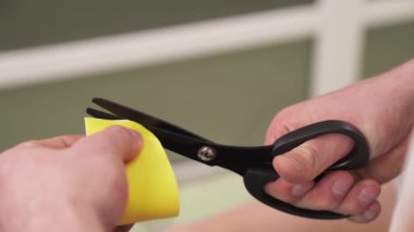 Sarı Kinesio bant ve makas kesiği olan bir erkek eli. Şeklini düzeltmek için köşeleri kesiyor. Kinesio bandının hazırlanması