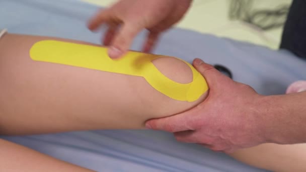 Fisioterapista Fissando Nastro Elastico Giallo Terapeutico Sul Ginocchio Dei Pazienti — Video Stock