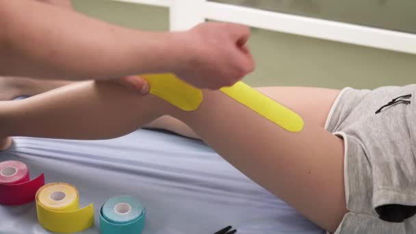 理学療法士は女性患者の膝から着物のテープを取り出します キネシオ療法と医療 — ストック動画