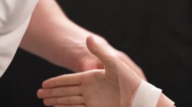 Bir terapistin beyaz spor bantlarını hastanın bileğine bantladığı bir gösteri videosu. Terapi ve rehabilitasyon