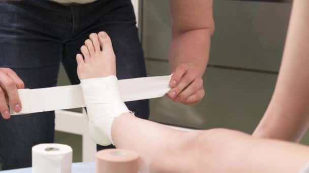 患者の足首の周りに医療用テープをテープセラピストのデモビデオ セラピーとリハビリテーション — ストック動画