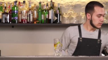 Barmen soda sifonundan buz küpleri, limon ve limon parçalarıyla dolu bardağa köpüklü su döker..