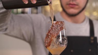 Kokteyl süzgecinden barmenin bardağa kokteyl döktüğü yakın çekim bir gösteri videosu. Profesyonel kokteyl yapımı..