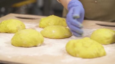 Mutfak eldivenleri giyen, hamuru yuvarlayan ve klasik ekmek somunları şeklinde şekillendiren bir fırıncı eli. Ekmek pişirme
