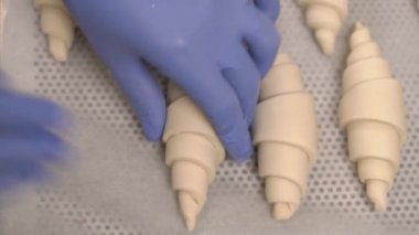 Pasta şeflerinin ellerinin hamur kruvasanları fırındaki bir tepsiye koyuşunun en üst görüntüsü. Yemek hazırlama.