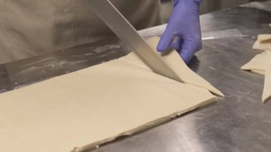 Fırıncıların el ele tutuşup kruvasan yapmak için hamuru üçgen dilimlere kestiği yakın plan bir fotoğraf.
