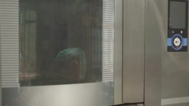 Üniformalı profesyonel bir fırıncı bir tepsi dolusu ham kruvasanı fırına koyuyor. Pastanede kruvasan imalatı.