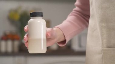 Hindistan cevizi sütüyle şişeyi tutup sallayan bir kadının yakın plan gösterimi. Ev yapımı sağlıklı yemek hazırlama