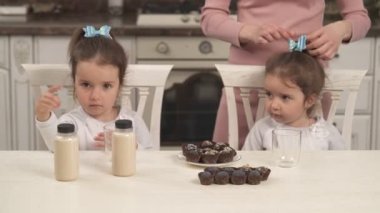 Çekici ikiz kızlar mutfak masasında oturup sağlıklı ve besleyici bir tatlı bekliyorlar. Ev yapımı hurma meyveleri ve badem sütlü kaju fıstığı şekerlemeleri. Vejetaryen, vejetaryen, sağlıklı gıda konsepti