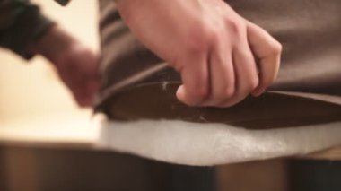 Mobilyacı kanepeye döşeme kuruyor. O, elle deri kumaşı sıkılaştırıyor. Fabrika atölyesine yakın çekim