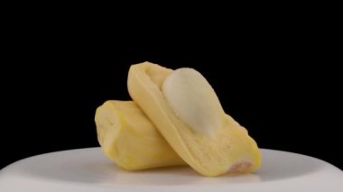 Beyaz pikapta dönen taze bir ekmek meyvesinin iki parçası. Siyah arkaplanda izole edilmiş.