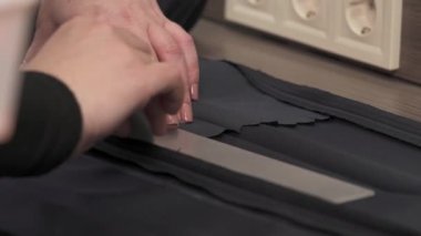 Profesyonel bir terzinin ellerinin malzemeyi ölçüp kesmeye hazırladığı yakın plan bir video..