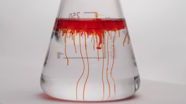 用纯透明液体将红色化学试剂滴入玻璃瓶中 锥形瓶中化学反应的特写 实验室测试 在白色背景下孤立无援 — 图库视频影像