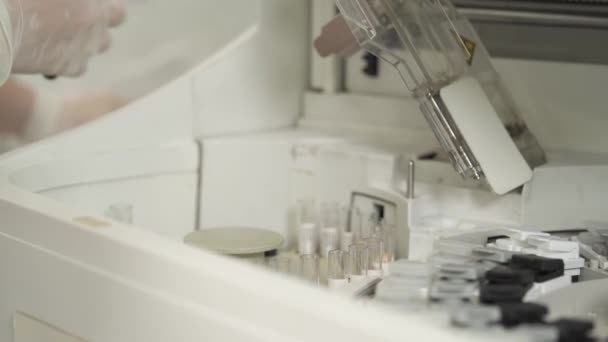 医学研究所の自動化化化化化化化化化学分析装置に生物試料を入れたチューブを置く医療技術者のクローズアップ — ストック動画