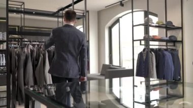 Erkek giyim mağazasının vitrininde şık gri ceketli bir adama bakan bir adamın gösteri videosu. Marka erkek kıyafetleri.