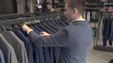 Erkek giyim mağazasının galerisindeki ceketlere bakan genç yakışıklı adam. Marka erkek takım elbise butiği.
