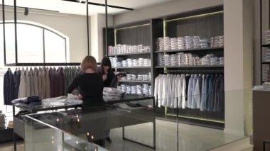 Tezgahtarların yeni erkek kıyafetleri koleksiyonunu raflara koydukları bir gösteri videosu. Moda mağazası rutin işleri. Yeni bir kıyafet koleksiyonu alınıyor.