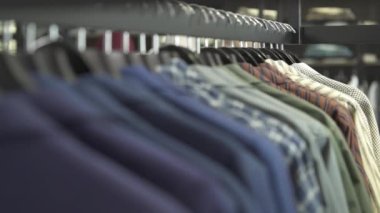 Dükkanda farklı erkek kıyafetleri olan askılar var. Odaklanma değişken çekim. Alışveriş ve satış konsepti.